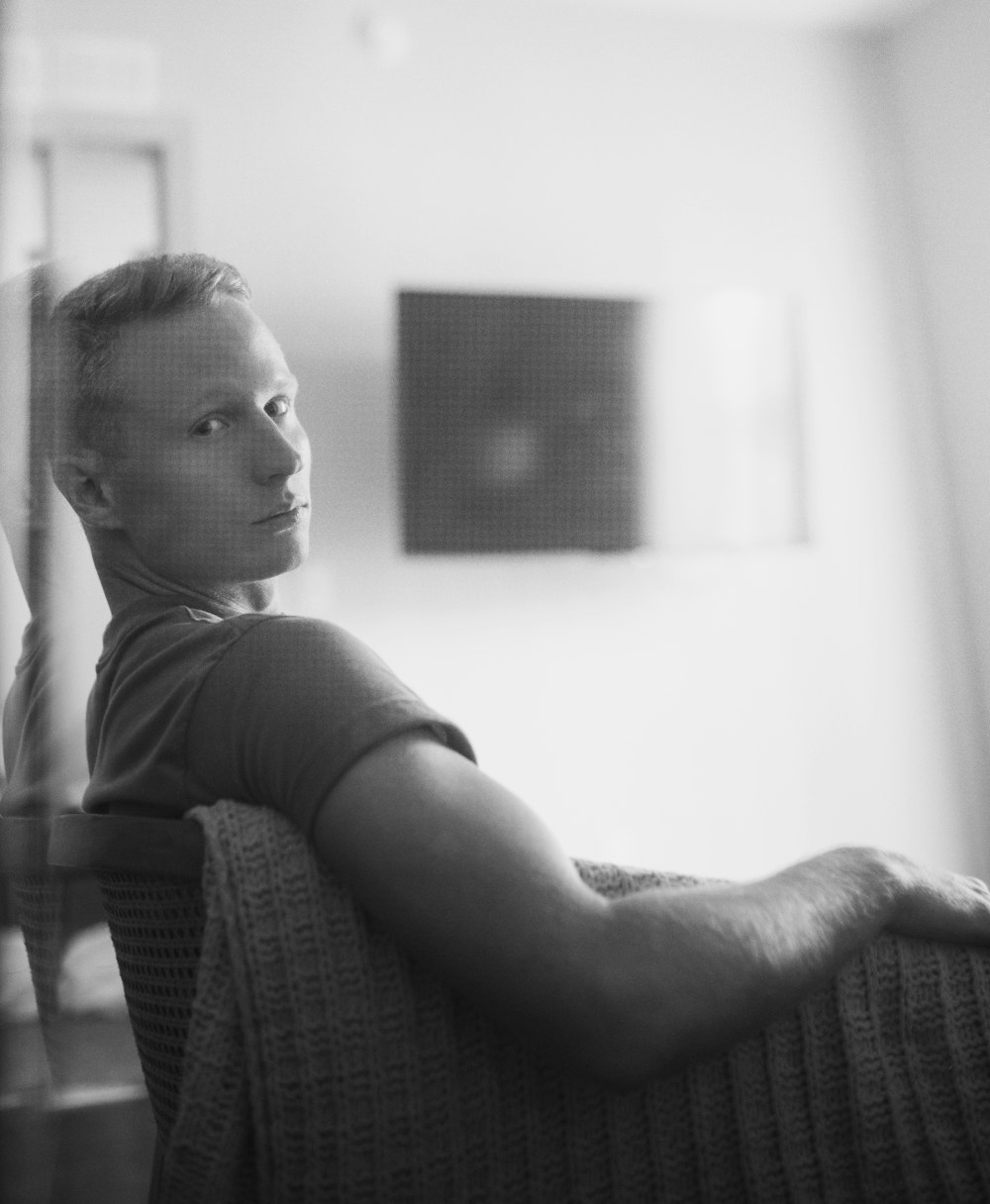 grayscale photo of boy in crew neck t-shirt sitting on chair