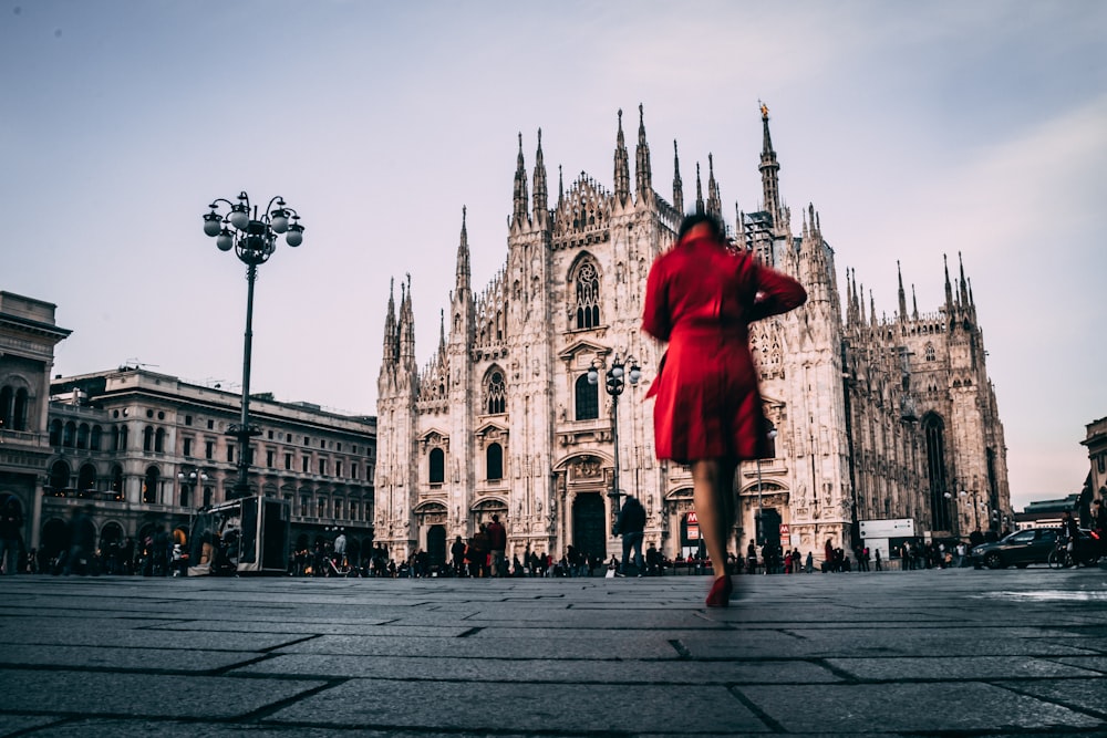 Femme en robe rouge debout sur un sol en béton gris près d’un bâtiment en béton brun pendant la journée