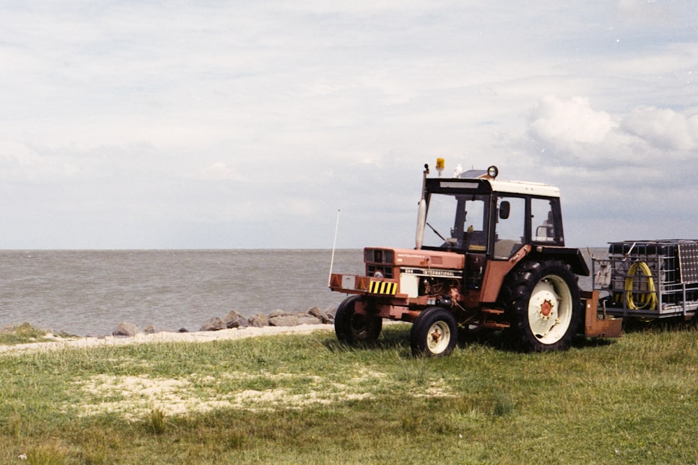 tracteur rouge et noir sur un champ d’herbe verte près de la mer pendant la journée