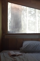 Dimly lit bedroom corner with wrinkled white sheets and an open poetry book, bathed in early morning light.