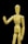 A wooden artist's mannequin is positioned against a black background. The mannequin is standing upright with one arm raised and bent at the elbow, as if gesturing or waving. The smooth, light wood of the mannequin contrasts starkly with the dark background.
