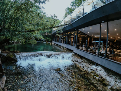 A serene riverside view of Nehirbahçe's outdoor dining area surrounded by lush greenery and a cascading waterfall.
