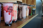 A colorful assortment of milk tea drinks with various toppings displayed on a wooden table.