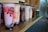 A row of assorted bubble tea cups sit on a wooden counter. Each cup contains different flavors and colors, with ingredients such as tapioca pearls visible at the bottom. The drinks are topped with plastic covers and have black straws wrapped in plastic.