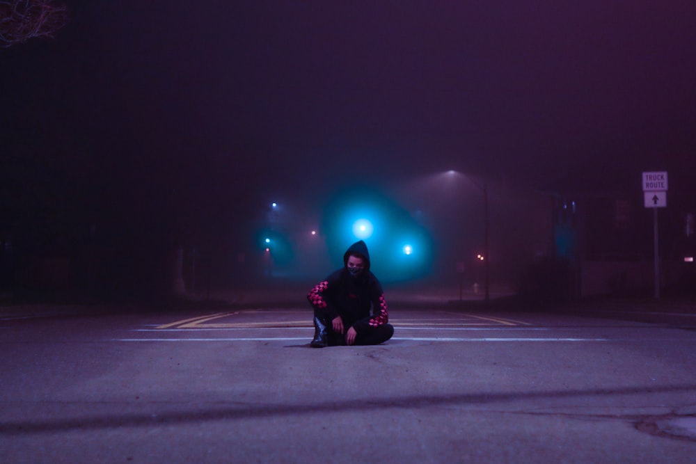 person in black jacket and pants sitting on road during night time