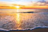Sunset over a tranquil beach with vibrant orange and pink hues reflecting on the water.