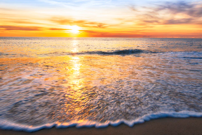 Sunset over the tranquil beach with vibrant orange hues reflecting on the water.