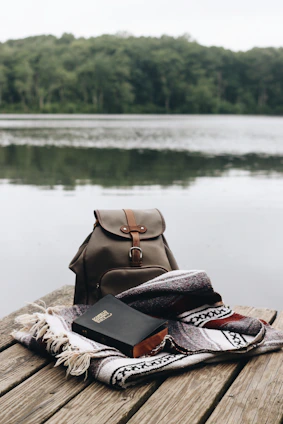 A serene sunrise over a quiet lake with an open Bible resting on a wooden dock.