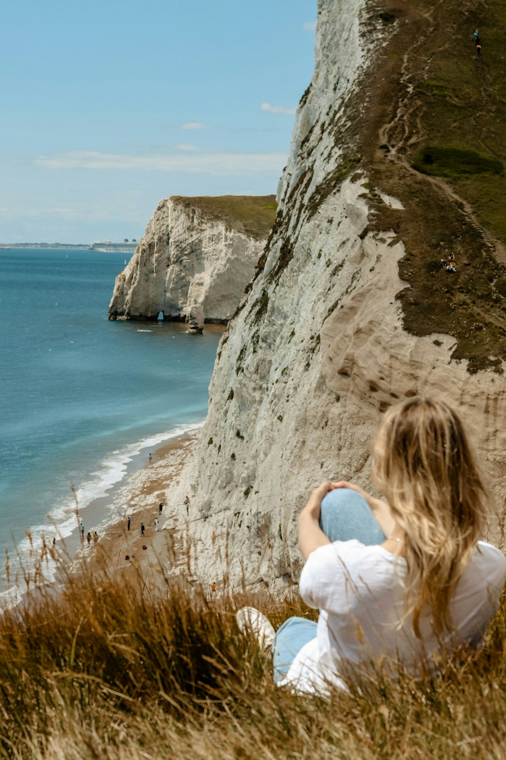 woman in white shirt sitting on rock formation looking at the sea during daytime