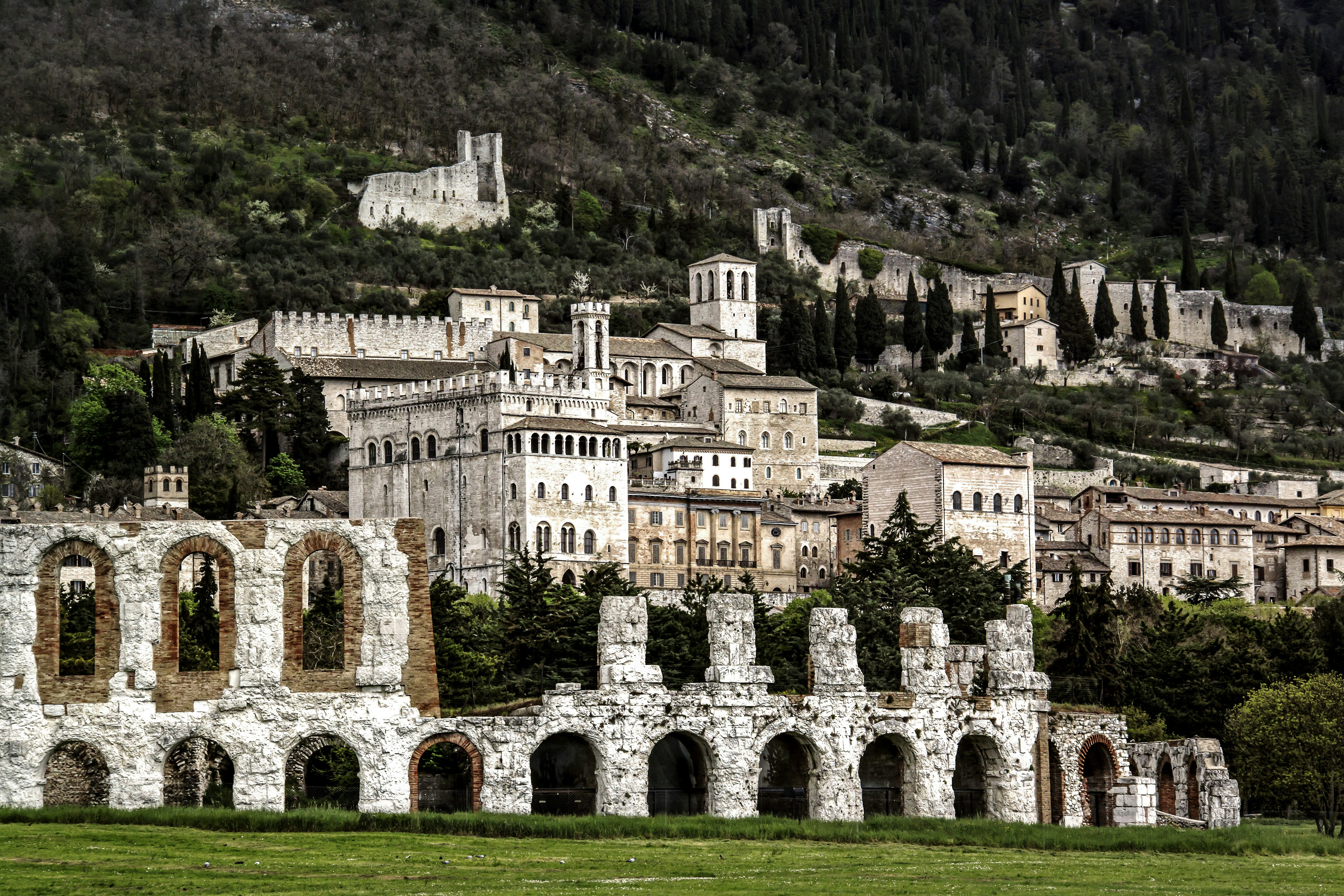 brown concrete building near green grass field during daytime, view of ancient roman amphitheater in front of hill town of gubbio