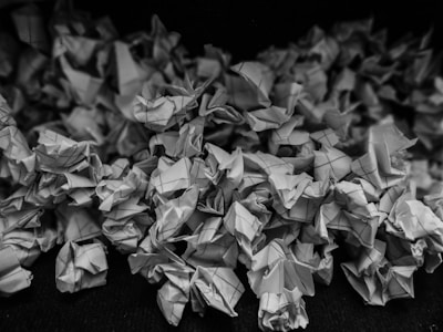 A collection of crumpled pieces of graph paper, all piled together creating a texture of folds and creases. The image is in grayscale, highlighting the intricate patterns and shadows formed by the overlapping papers.
