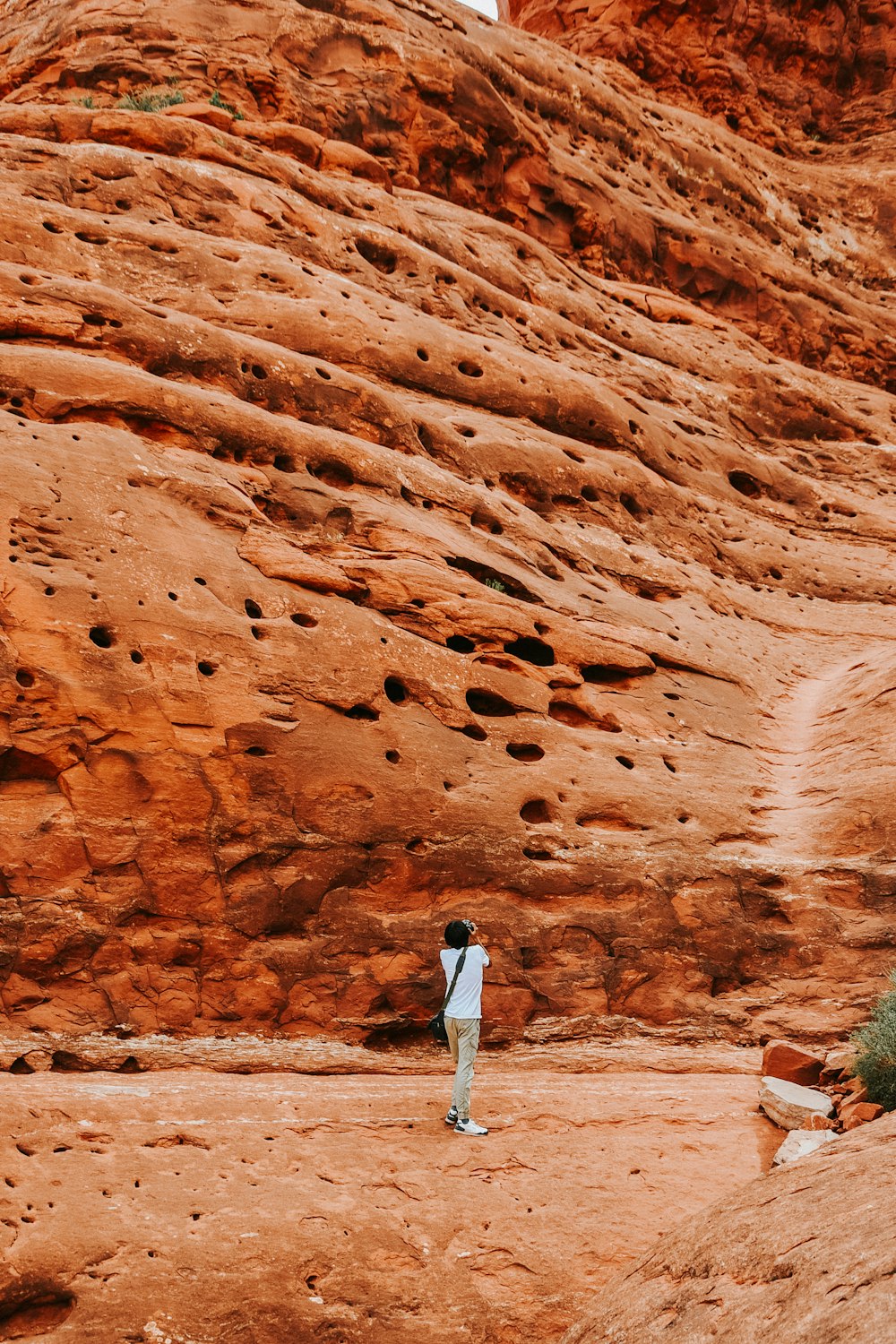 白い長袖シャツと白いズボンを着た女性が昼間、茶色の岩層の上に立っている