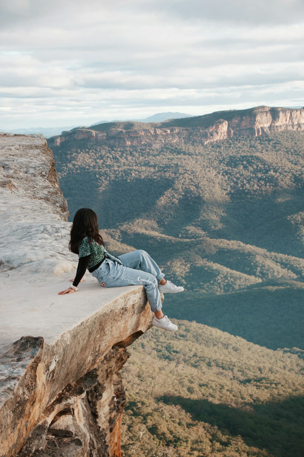 woman in blue denim jeans sitting on brown rock formation during daytime