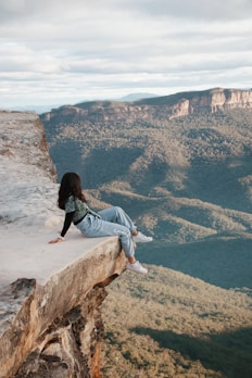 woman in blue denim jeans sitting on brown rock formation during daytime