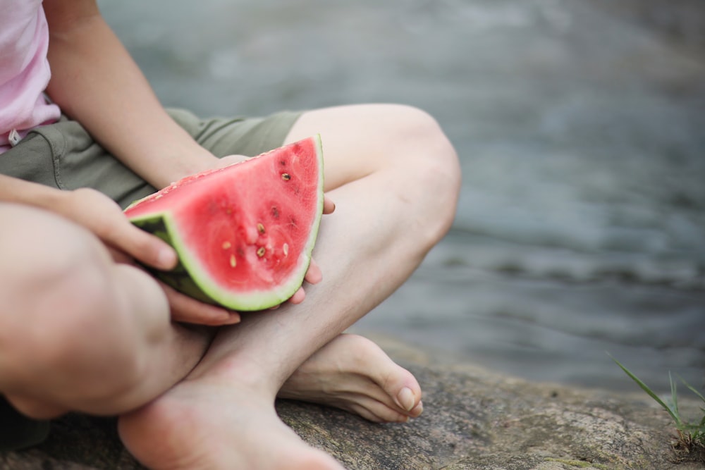person holding sliced watermelon on brown sand during daytime