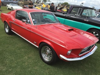 A gleaming vintage red, white, and blue classic car at an outdoor American car show with a patriotic crowd admiring the vehicles.