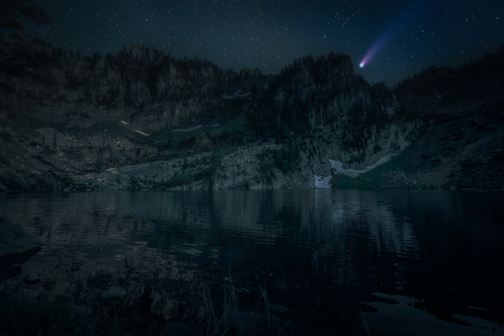 body of water near trees and mountain under blue sky during night time