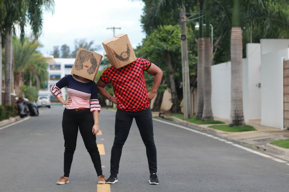 man and woman holding brown cardboard box walking on the street during daytime