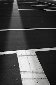Worker applying black sealcoat evenly over a commercial parking lot under bright sunlight.
