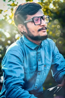 Close-up of a happy man with glasses and a beard, outdoors with soft sunlight in the background.
