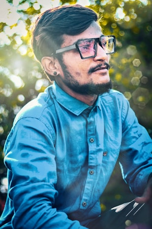 Close-up of a happy man with glasses and a beard, outdoors with soft sunlight in the background.