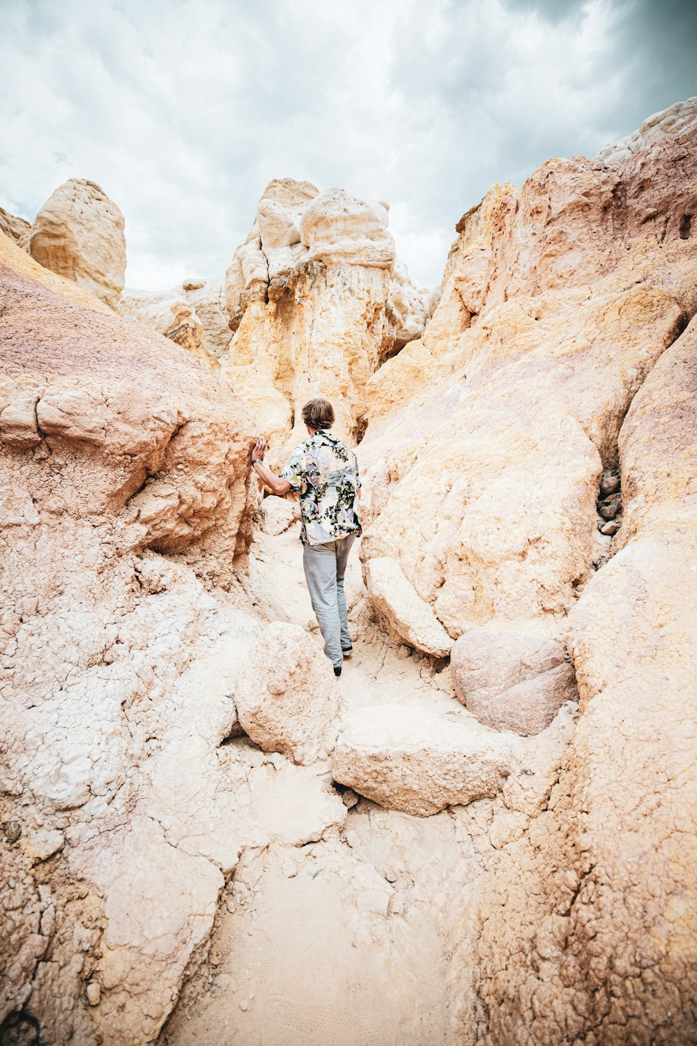 man in white t-shirt and blue denim jeans standing on brown rock formation during daytime