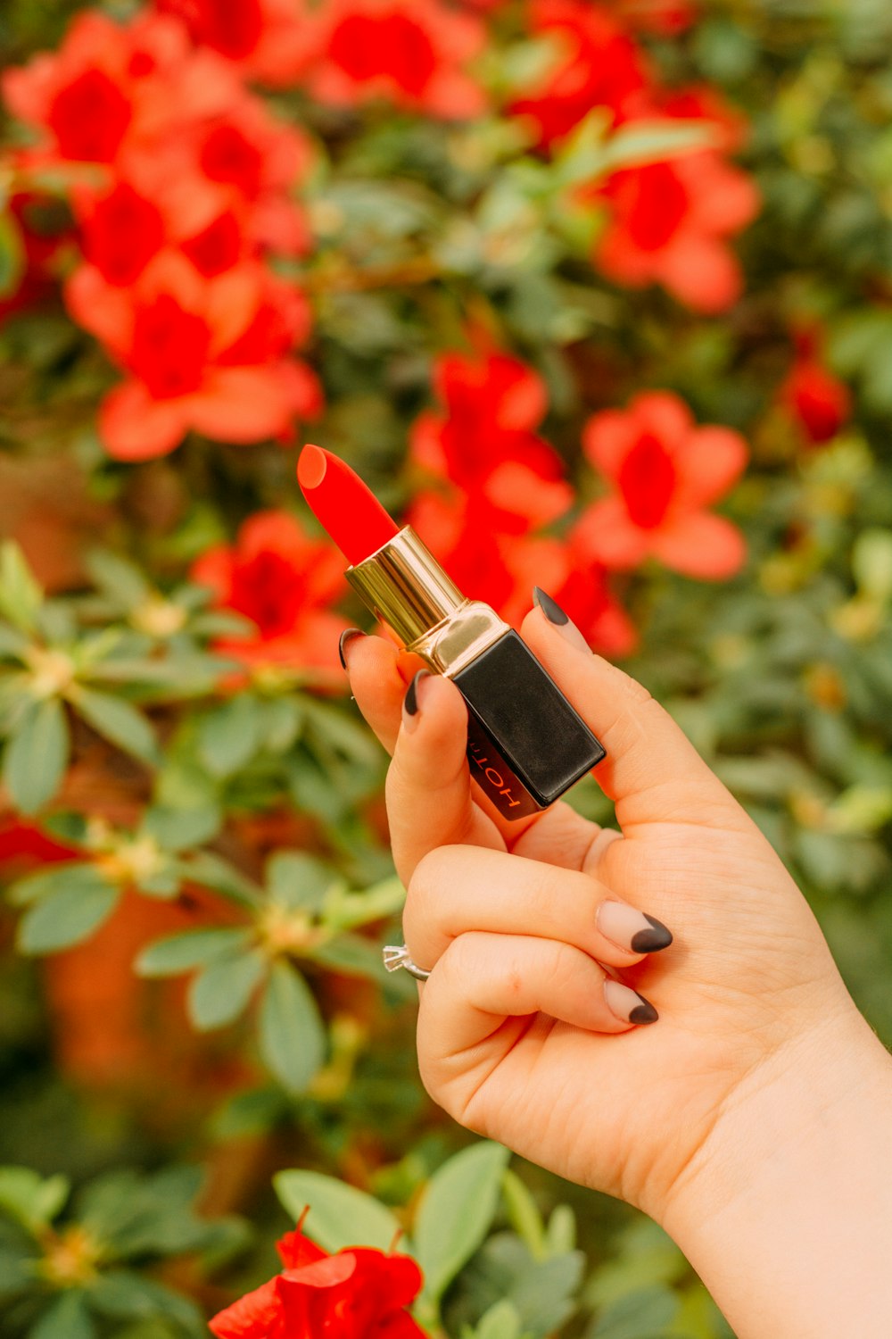 person holding red lipstick near red flowers