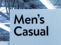 A signage featuring bold, black text reads 'Men's Casual' against a light background. The setting appears to be indoors, with visible overhead lighting and structural elements like beams creating an industrial look.