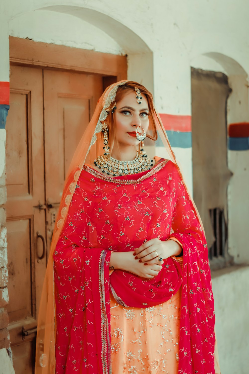 woman in red and white floral sari standing near brown wooden wall during daytime