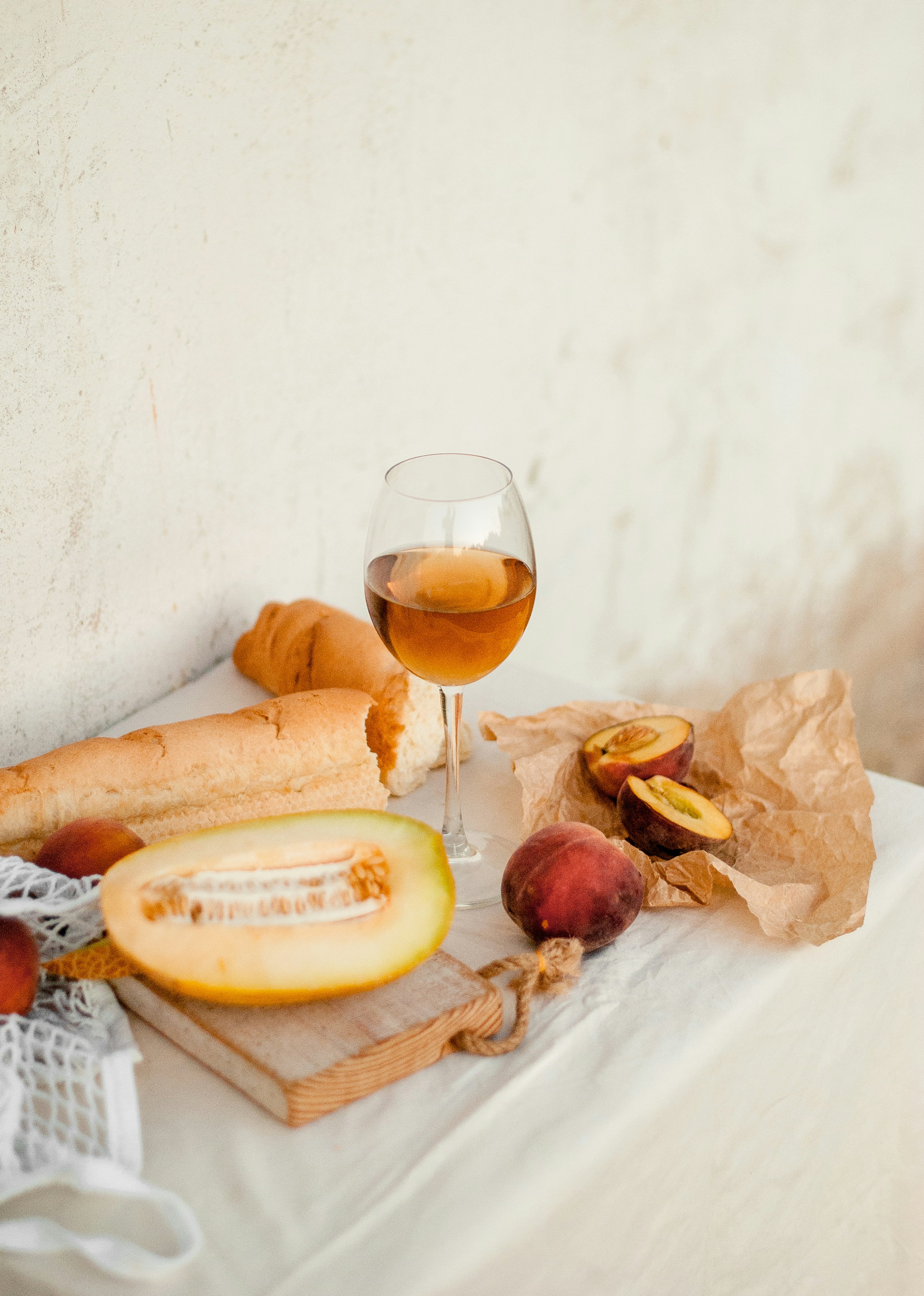A glass of wine, peaches, and a cut melon on a table.