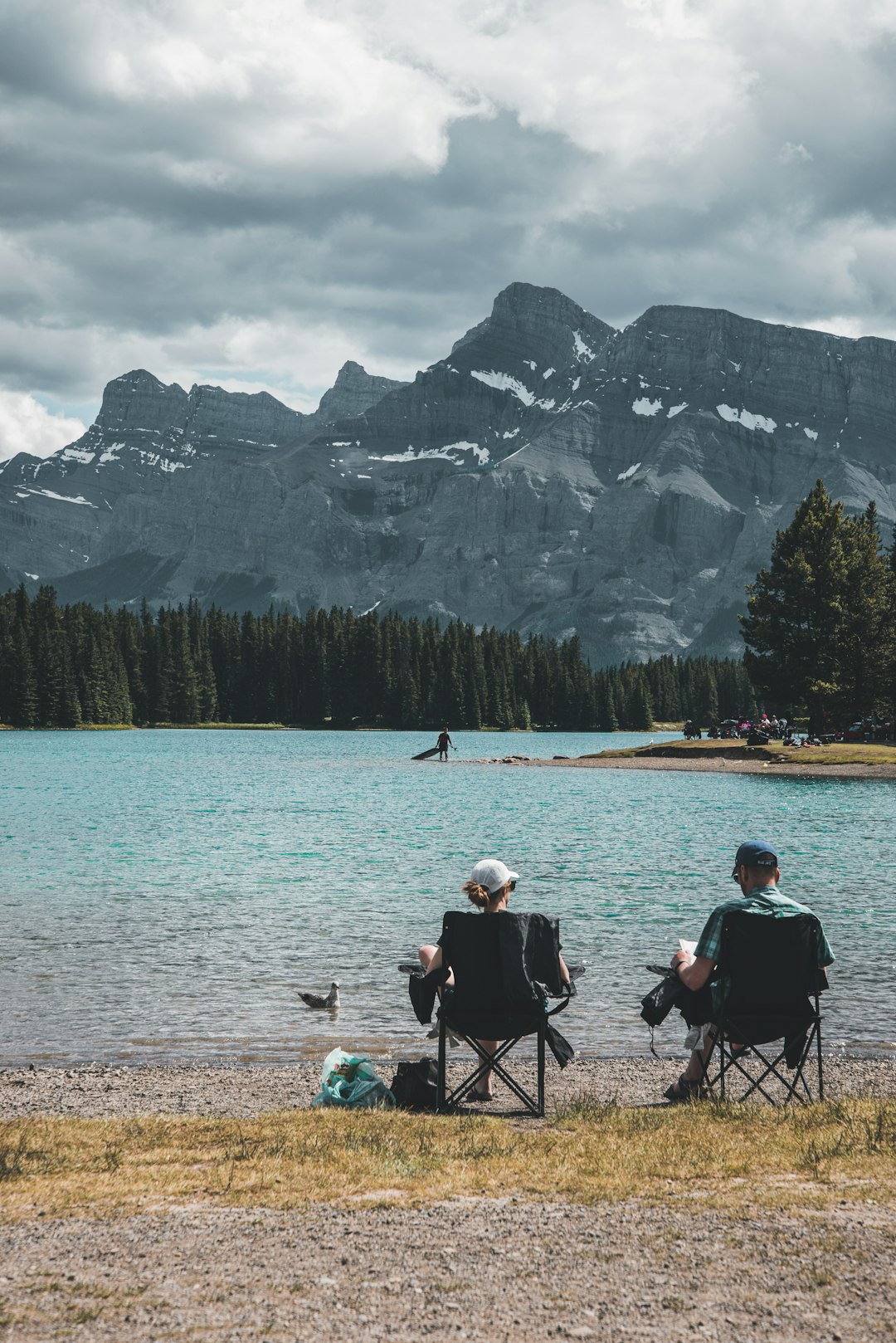 people sitting on camping chairs near lake and snow covered mountain during daytime