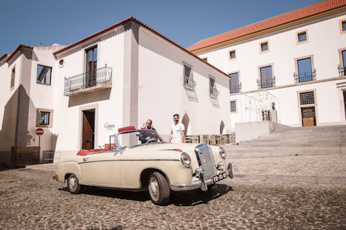 A classic convertible parked beside a cobblestone street lined with historic buildings.