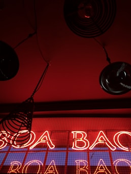 Bright red neon lights spell out the words against a dark background with black circular metal objects hanging from the ceiling, creating a bold, modern, and industrial aesthetic.
