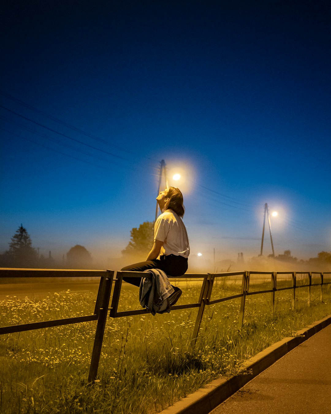 man in white shirt sitting on black metal fence during night time