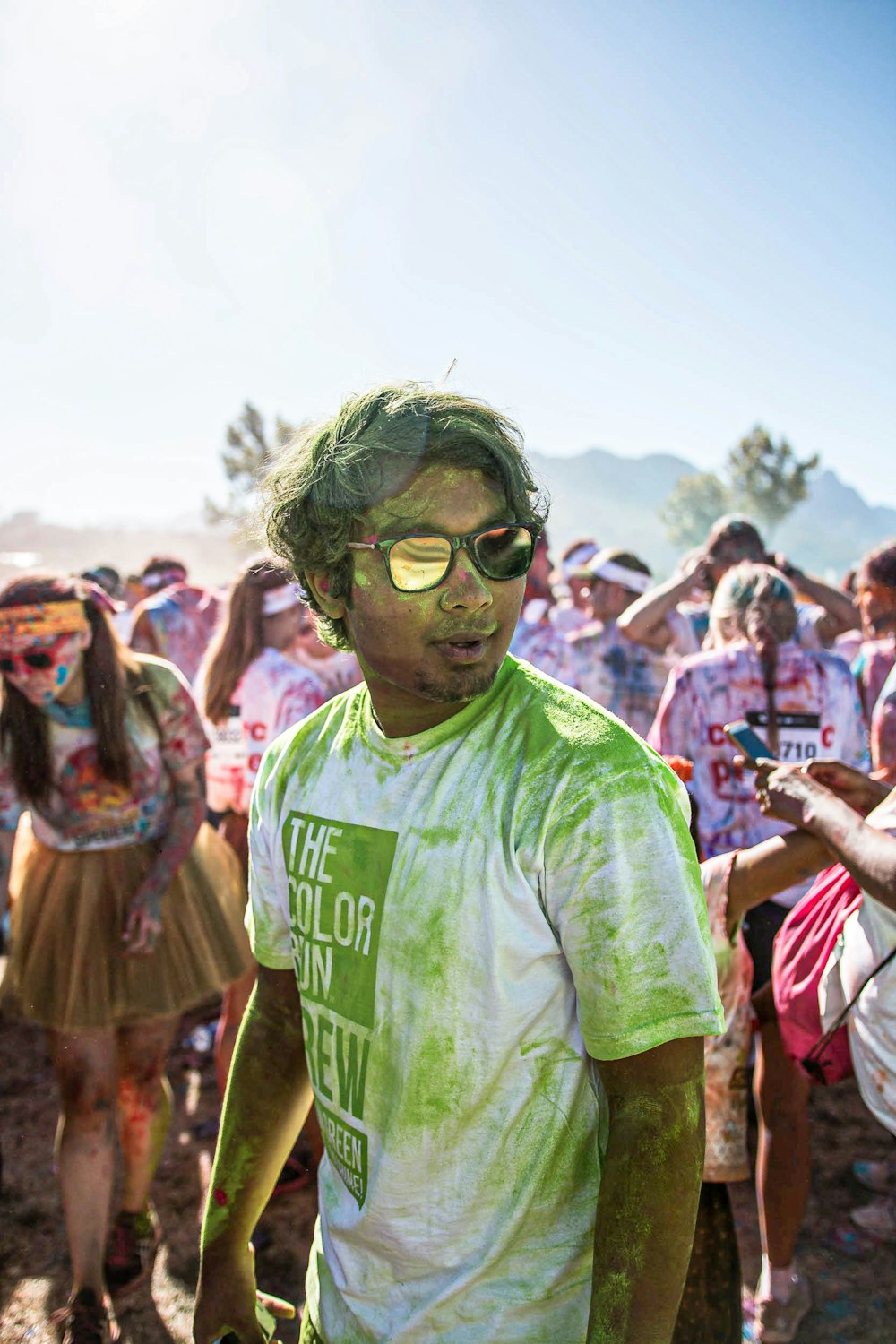 Mann im grünen Rundhals-T-Shirt mit Sonnenbrille, der tagsüber in der Nähe von Menschen steht
