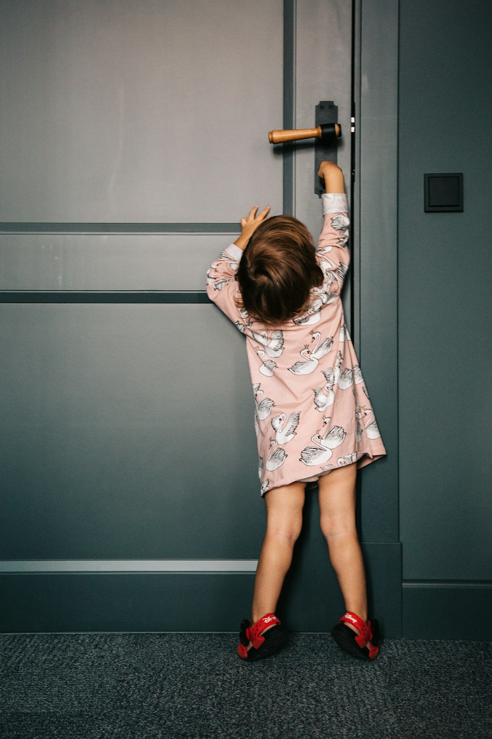 girl in white pink and green floral dress standing beside gray wall