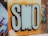 Bold graffiti art featuring large, stylized letters 'SMO' painted in pastel blue with a dark outline against an orange and yellow gradient background. The surrounding wall has additional graffiti with various colors and designs. The phrase 'smile more often...' is written in white on the left, adding a positive note.