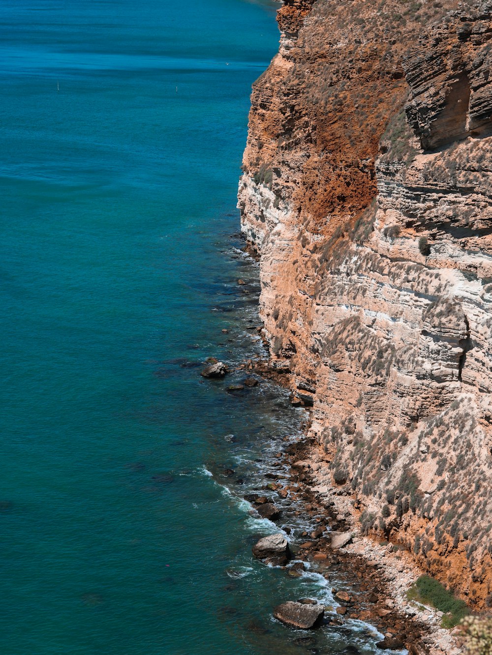 brown rocky mountain beside blue sea during daytime