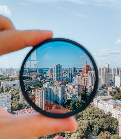 person holding round mirror with city buildings in the distance