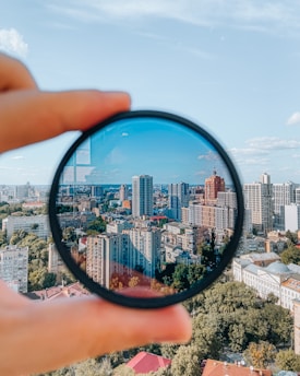 person holding round mirror with city buildings in the distance