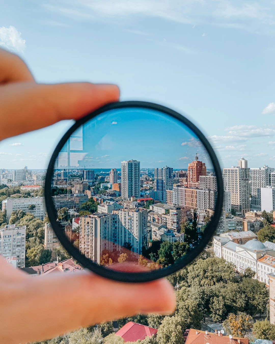 person holding round mirror with city buildings in the distance