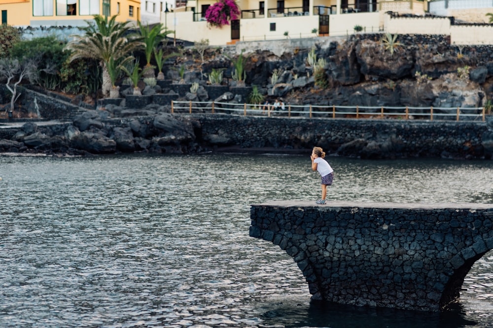 woman in white t-shirt and black shorts standing on concrete dock during daytime