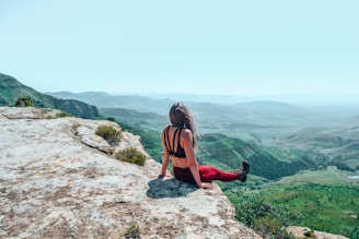 woman in red tank top sitting on rock during daytime