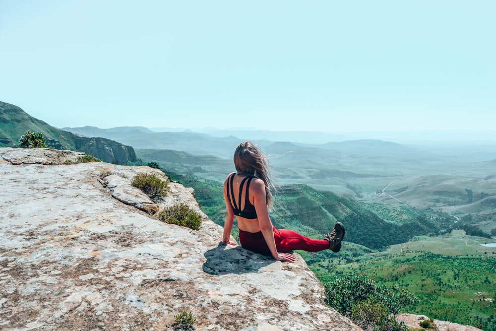 woman in red tank top sitting on rock during daytime