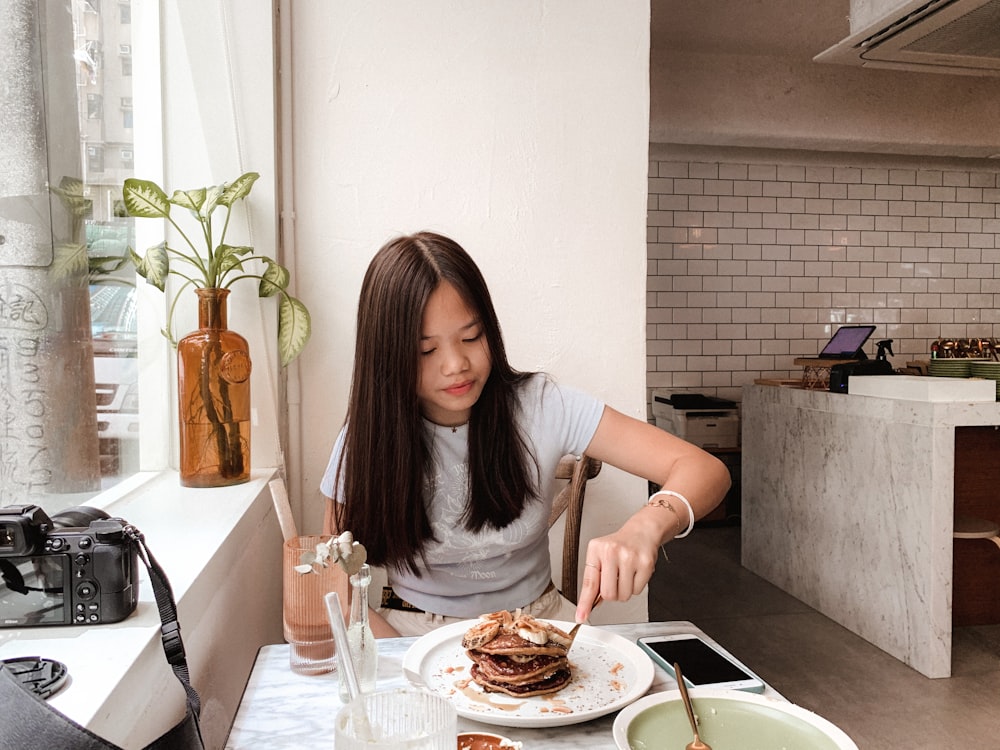 Mujer con camisa gris sentada en una silla frente a la mesa con comida