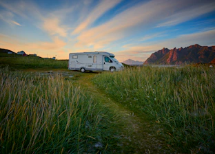A cozy camper van parked by a vibrant sunset overlooking a mountain range.