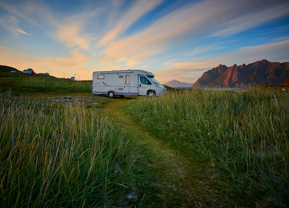 furgone bianco sul campo di erba verde vicino alla montagna marrone sotto il cielo blu durante il giorno