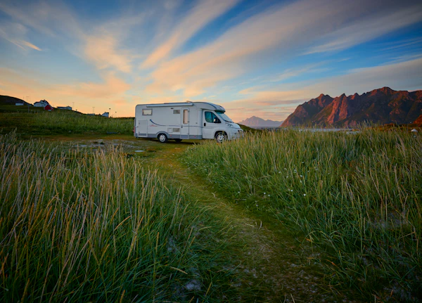 White campervan on a green grass field below a brown mountain and blue sky