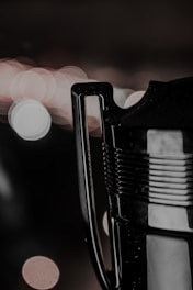 A close-up of a trophy handle with a blurred, bokeh-lit background featuring circular light patterns. The metallic surface of the handle and part of the trophy is visible, reflecting some of the light.
