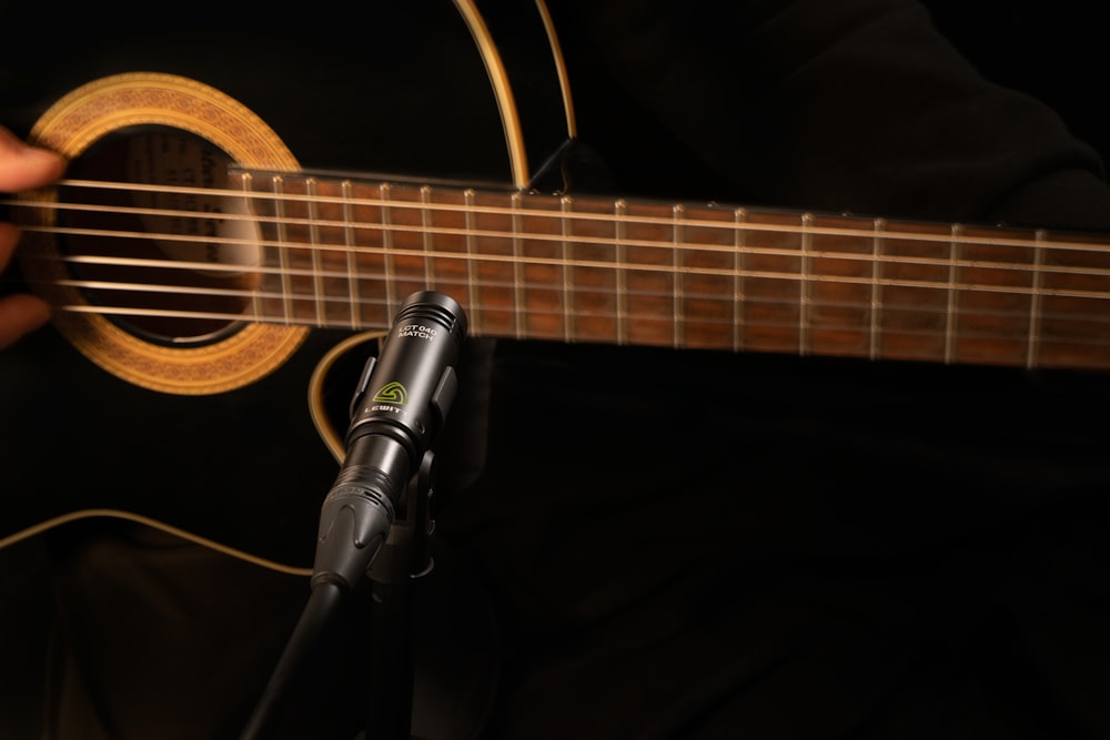 brown acoustic guitar beside black microphone